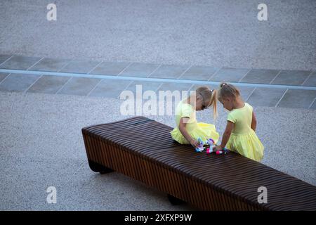 Twin sisters playing together on bench in park Stock Photo