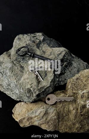 3 keys one old style 2 modern laying on rocks with black background, still life. Stock Photo