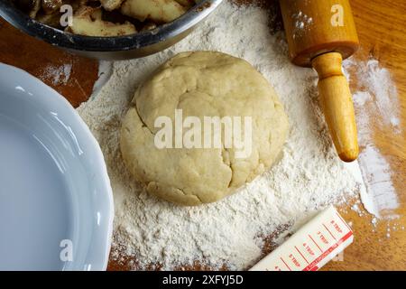 Making a pie.  Getting ready to make a pie.  Dough on a floured wooden surface.  Top down view includes: pie plate, rolling pin, butter, and sliced pr Stock Photo
