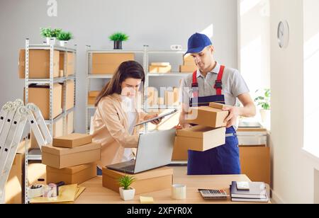 Man from delivery service working in warehouse with female small business owner in logistics center Stock Photo
