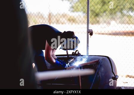 A welder at work with protective gear and a welding torch in an outdoor setting Stock Photo