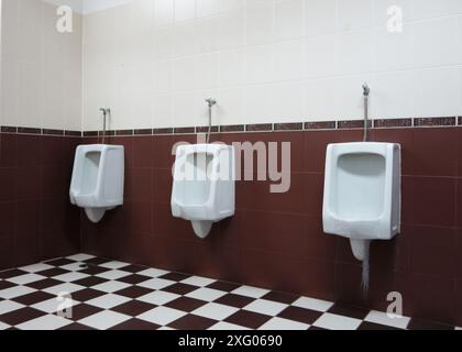 White urinals in the men's bathroom with tiled wall. Stock Photo