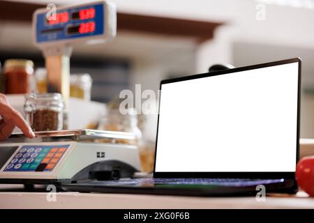 Close-up of laptop at cashier desk, showing isolated chromakey copyspace template. In local eco friendly market, digital laptop displaying blank white screen for advertising. Stock Photo