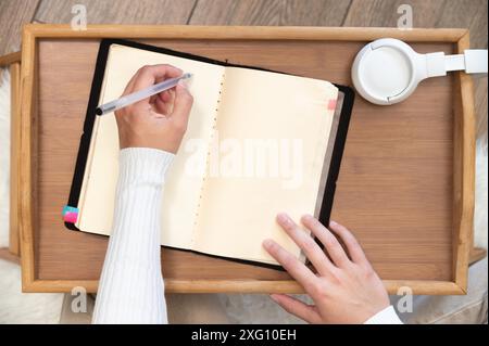 Top view Close-up of female hands writing with gel black pen in leather notepad on wooden table at home Stock Photo