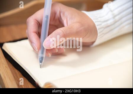 Close-up of female hands writing with gel black pen in leather notepad on wooden table at home Stock Photo