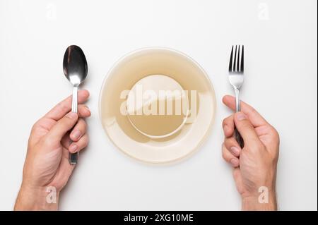 Fork and spoon in male hands at an empty plate in anticipation, a hungry client, white isolated background Stock Photo