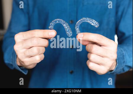Caucasian young man shows invisible aligner for teeth correction. A man's hand holds plastic braces for dentistry to straighten his teeth, against Stock Photo