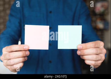 Men's hands in a shirt hold multi-colored squares of note paper, blank stickers, on a blurred background. office worker Stock Photo