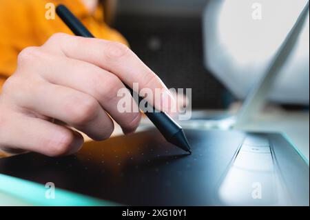 Casual man, freelancer with stylus, writing on digital tablet screen, working on laptop computer at office desk. Graphic or web designer working on Stock Photo