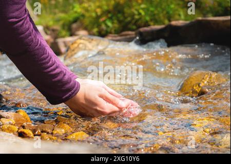 Female hands close-up draw water from a mountain stream to quench thirst, drink from a clean source of water. tourist on a hot sunny day Stock Photo