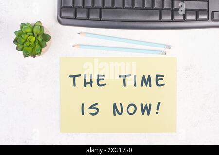 The phrase the time is now is standing on a paper, a pen, computer keyboard and a cactus, brainstorming for new business ideas, startup concept, home Stock Photo