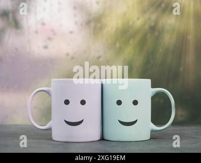 Happy, similing face, mug couple on a window sill cuddle, cup of coffee on a rainy day, support, relationship and friendship concept Stock Photo