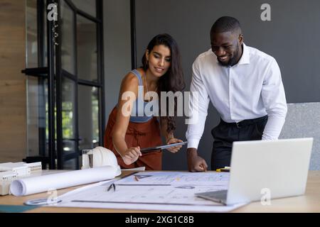 Collaborating on project, colleagues reviewing blueprints and using tablet in office Stock Photo
