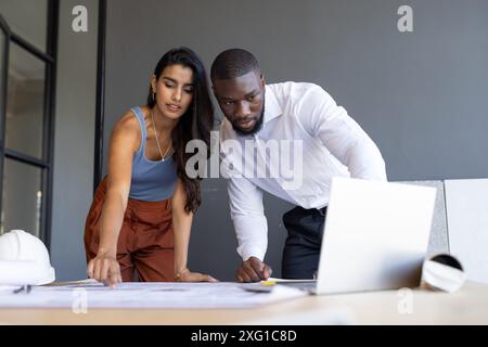 Collaborating on project, colleagues reviewing blueprints and using laptop in office Stock Photo