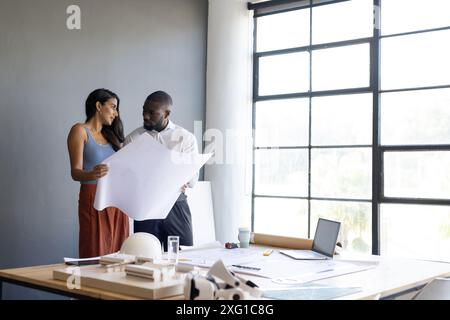 Architects reviewing blueprints in office, discussing project details near window, copy space Stock Photo