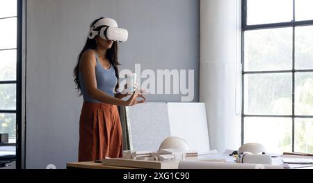Using VR headset, woman holding coffee cup and working on architectural model, copy space Stock Photo