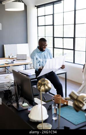 Reviewing architectural plans, man sitting at desk in modern office workspace Stock Photo