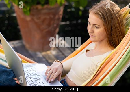 Relaxing in hammock, woman using laptop for work or leisure outdoors Stock Photo