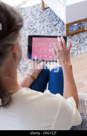 Using tablet, senior woman controlling smart home features in living room Stock Photo