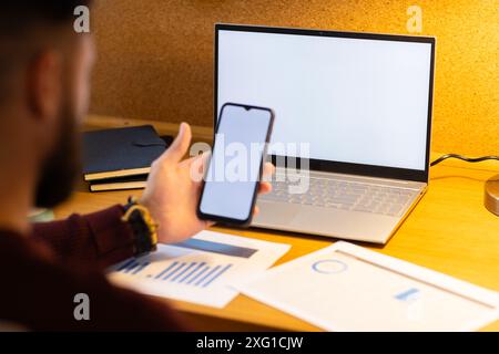 Using smartphone and laptop, man working from home with documents on desk, copy space Stock Photo