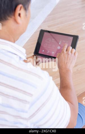 Using tablet, senior man controlling smart home devices with touchscreen interface Stock Photo