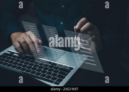 A person is typing on a laptop with a pen in front of them. The laptop screen shows a series of check boxes and a person is writing on it. Scene is fo Stock Photo