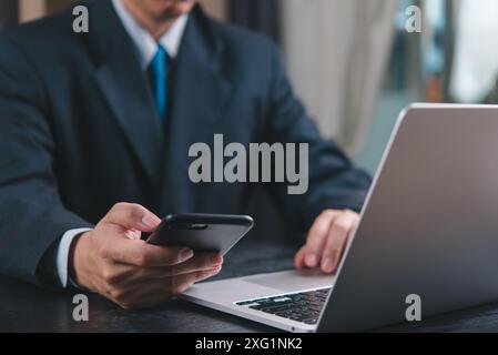 Businessman using phone and laptop simultaneously. Concept of multitasking, modern work environment, professional communication. Ideal for corporate, Stock Photo