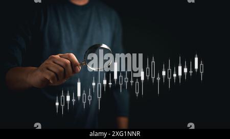 Businessman holding a magnifying glass over financial data charts, symbolizing detailed financial analysis. Highlights market research and investment Stock Photo