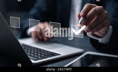 A businessman interacts with a digital checklist on a laptop, symbolizing task management and efficiency in a modern office. Stock Photo