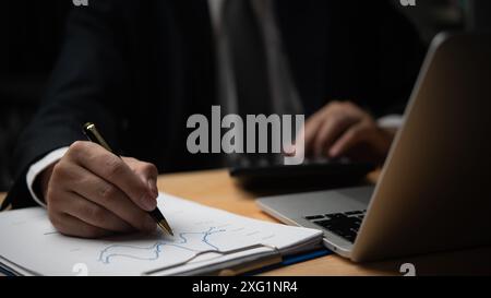 Businessman writing on financial charts, using calculator. Detail-oriented work in finance, accounting. Perfect for business management, financial pla Stock Photo