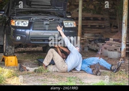Father teaching son car repair auto mechanics underneath car in shop Stock Photo