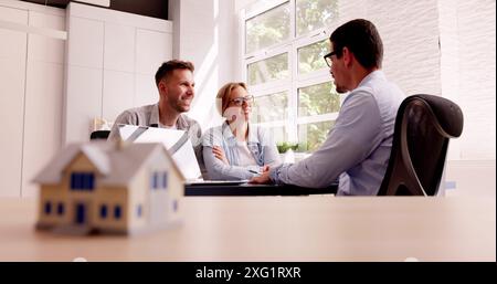 Corporate Architect Presenting Renovation Plans To Young Couple On Laptop in Office, discussing family house project with estate agent. Stock Photo