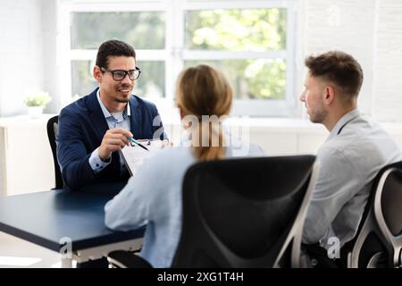 Financial consultant explaining new project investment to young couple in office. Real estate agent discussing mortgage options with family. Mortgage Stock Photo