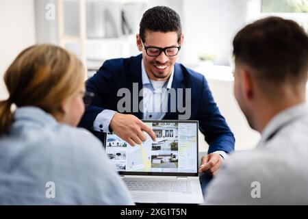Professional Real Estate Agent Presenting Property Options to Happy Couple Using Laptop in Modern Office Setting Stock Photo