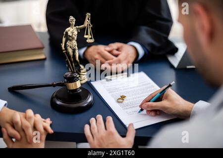 Young couple, one Caucasian and one Hispanic, consulting with a lawyer in court to sign a divorce agreement document. Stock Photo