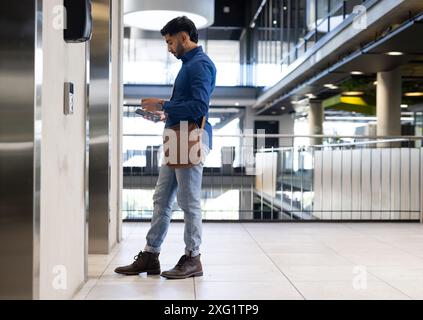 Businessman using smartphone and waiting for elevator in modern office building, copy space Stock Photo