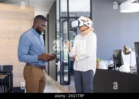 Using VR headset, woman gesturing while man holding tablet in modern office Stock Photo