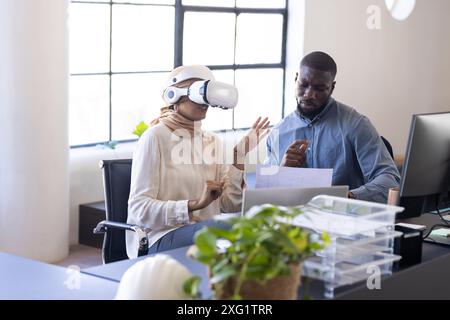 Using VR headset, business colleagues discussing project at office desk Stock Photo