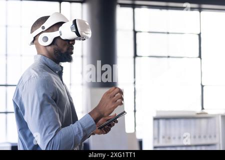Using VR headset, man interacting with virtual environment while holding tablet Stock Photo