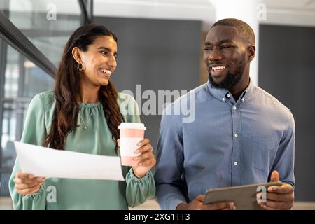 Holding coffee cup and documents, woman talking with man holding tablet in office Stock Photo