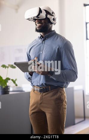 Using VR headset, businessman holding tablet and smiling in modern office Stock Photo