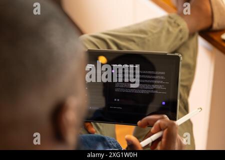 Using AI chatbot on tablet and stylus, man reading about implementing CRM system at home Stock Photo