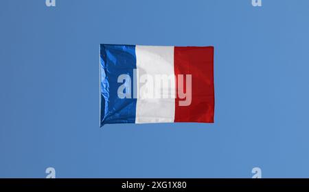 Large French flag hangs suspended in the blue sky seemingly unsupported Stock Photo