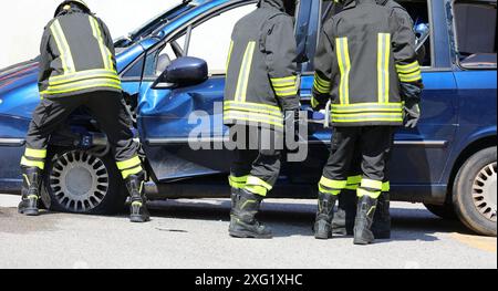 team of firefighters using hydraulic shears and jaws of life to pry open the door of a crashed car after an accident in order to extricate the injured Stock Photo