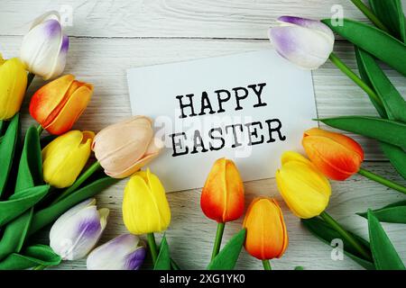 Happy Easter text message on paper card with tulip flowers top view on wooden background Stock Photo
