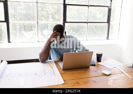 Working at desk, man using laptop and reviewing architectural blueprints Stock Photo