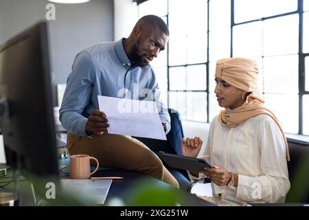 Discussing project, colleagues reviewing blueprint and using tablet in modern office Stock Photo