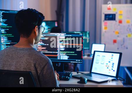 Asian software developers working on multiple screens displaying code and application diagrams at night in modern office Stock Photo