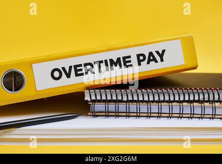 Overtime pay written on the label of a yellow binder on the office desk. Business employee overtime payment and staff payroll concept. Stock Photo
