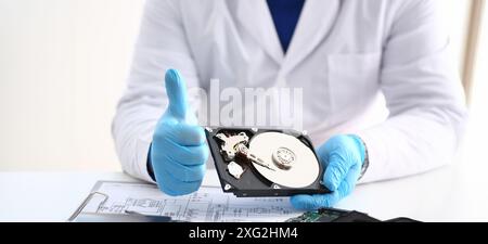 Man in uniform hold disassembled hard drive from computer, hdd and reader, show thumbs up Stock Photo